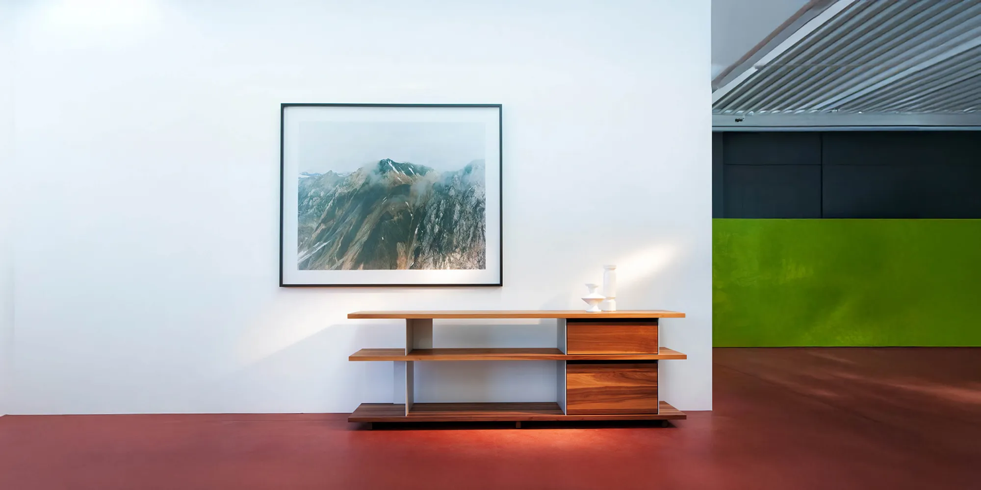 Strakke omgeving waarin een schilderij te zien is op een witte muur. Voor de muur staat een Girsberger kastje op een rode vloer.